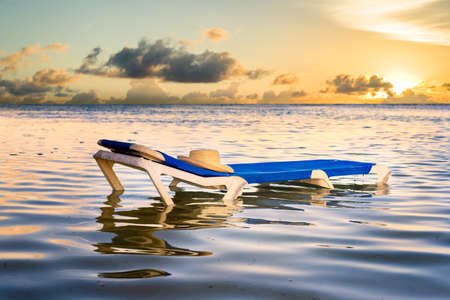 Blue lounge chair resting in the peaceful Caribbean Sea bathed in golden sunset lightの写真素材