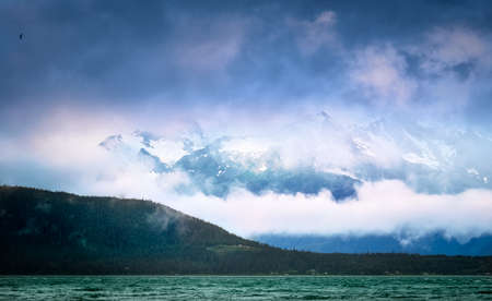 Clouds and fog covering the snow-capped mountain peaks over the inlet at Skagway, Alaskaの写真素材