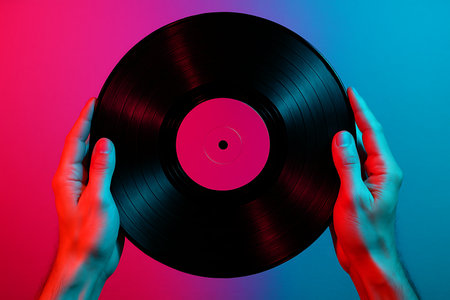 Close-up shot of two hands holding a black vinyl record against a vibrant pink and blue neon background. The image evokes a retro, music-themed aesthetic.の素材