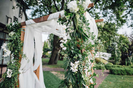 Wooden ceremony arch decoretade by white cloth, flowers and greenery standing in bright garden for wedding ceremony. Decor.の写真素材
