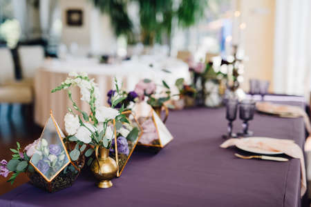Composition of flowers in florariums standing on table covered by violet cloth and decorated by candles and cutlery. Decor. Wedding. Receptionの写真素材