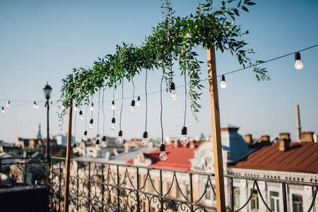 Lamps, green garland hang over the balcony on the top of the roof. Wedding decor