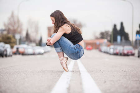 woman dancer on ballet tips and jeans on the street and hugging his knees and look down