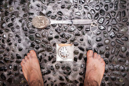 View of a man's feet while taking a shower copper floor of black stonesの写真素材