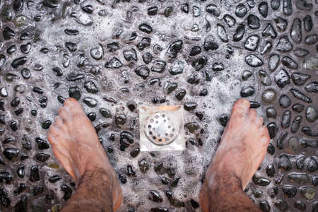 View of a man's feet while taking a shower copper floor of black stonesの写真素材