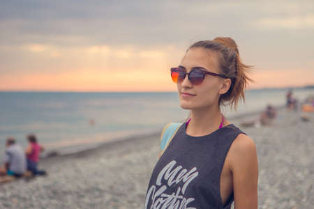 Sunset dawn. Young woman standing on a rounded pebble stones. The girl enjoys the unusual beach, pebbles on the shore of the Black seaの写真素材