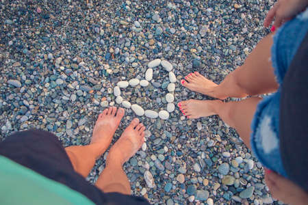 Young woman and boy standing on a rounded pebble stones. A girl and a boy enjoying an unusual beach, pebbles on the shore of the Black sea heartの写真素材