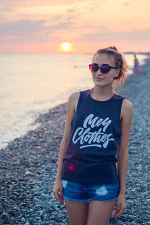 Sunset dawn. Young woman standing on a rounded pebble stones. The girl enjoys the unusual beach, pebbles on the shore of the Black seaの写真素材