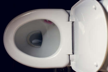 White toilet bowl in a bathroom with black backgroundの写真素材