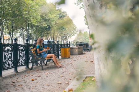 the girl sitting on the bench with the phone. Beautiful young woman on the bridge of peace in Tbilisi, Georgia old town cityの写真素材