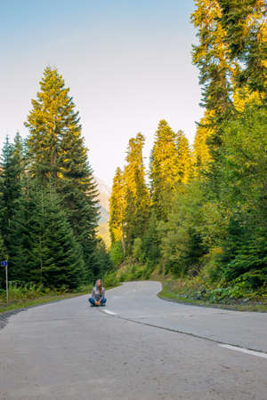 Beautiful young woman sitting on the road and looking forward. Around the forest. Serpentineの写真素材