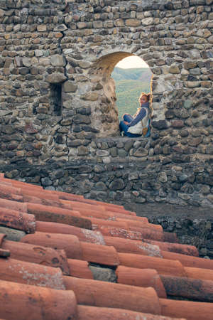 The girl with the backpack vest. Sitting in the window of the fortress, looking at the sunrise tavern. Tourist travelerの写真素材