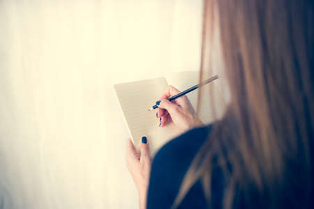 Beautiful woman in a black dress with an open notebook with pen and pencil, Studio isolated on white backgroundの写真素材