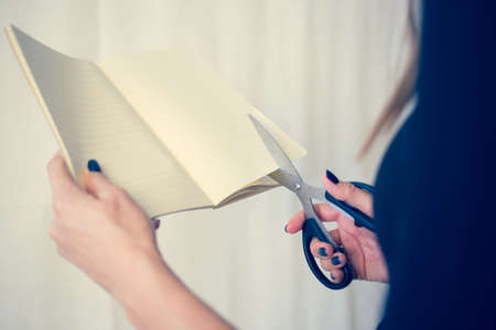 Beautiful woman in a black dress with an open notebook with a pair of scissors cuts, Studio isolated on white backgroundの写真素材