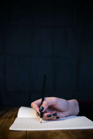 Beautiful woman in a black dress with an open notebook with pen and pencil, Studio isolated on black backgroundの写真素材
