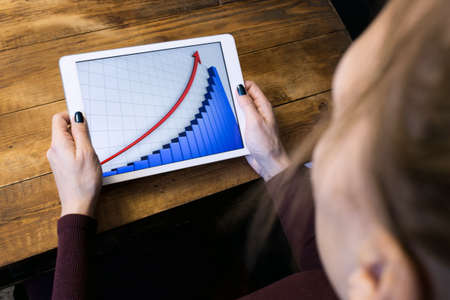 The girl working with a tablet computer. The graph rises. Table, wooden, background black