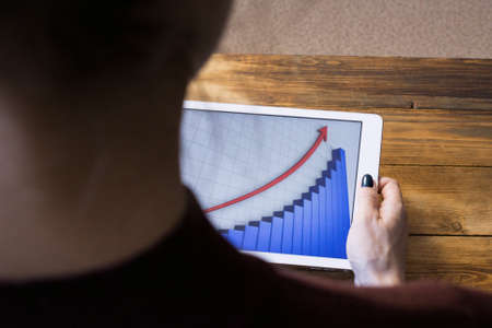 The girl working with a tablet computer. The graph rises. Table, wooden, background blackの写真素材
