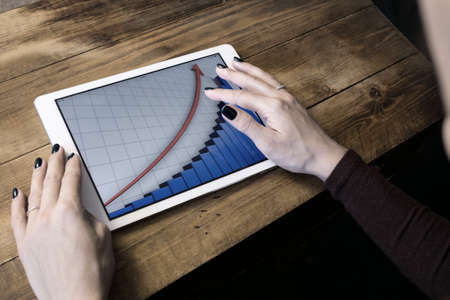 The girl working with a tablet computer. The graph rises. Table, wooden, background blackの写真素材