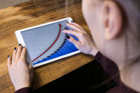 The girl working with a tablet computer. The graph rises. Table, wooden, background blackの写真素材