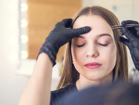 Master makeup corrects, and gives shape to pull out with forceps previously painted with henna eyebrows in a beauty salon. Professional care for face.の写真素材