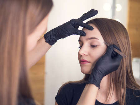 Artistic correction of eyebrows of a young girl. professional make-up in the beauty salon master makes a professional fresh summer make-up of a beautiful model in the salonの写真素材