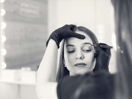 Master makeup corrects, and gives shape to pull out with forceps previously painted with henna eyebrows in a beauty salon. Professional care for face.の写真素材