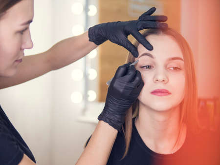 Artistic correction of eyebrows of a young girl. Tweezers, forceps. Beautiful Woman with long eyelashes in a beauty salon. Eyelash extension procedure. Lashes close upの写真素材