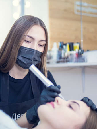 Master at work with the eyebrows makes microbleeding tattoo . Microblading eyebrows workflow in a beauty salon. Light brown girl do eyebrows needle.の写真素材