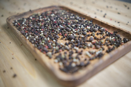A mixture of Indian seasonings is poured into a wooden plate on a wooden table. Black pink pepper....