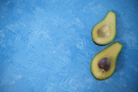 Food background with fresh organic avocado on a blue background painted with oil paints. top view, Two halves.の写真素材