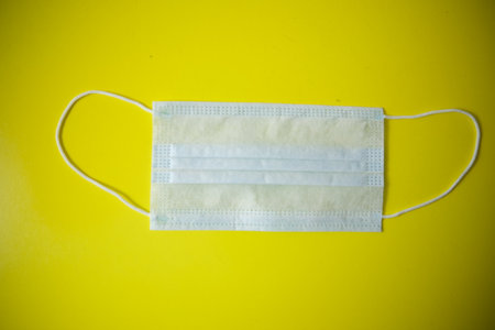 Protective medical mask on the table. The background is yellow with art paint. Lying carelessly.の写真素材