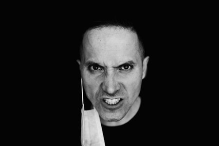 Aggression. A black and white photo of an angry man. Protective medical mask on the ear. He grins....
