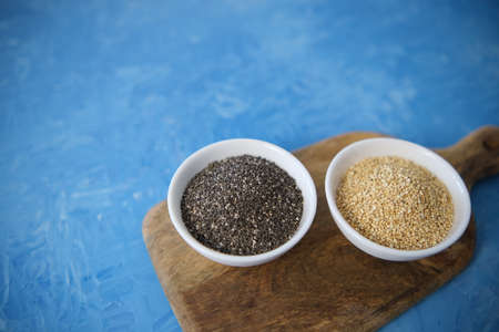 Quinoa and chia seeds are organic food for a healthy diet. In a round bowl. Two white cups. The blue texture is painted with blue oil paints.の写真素材