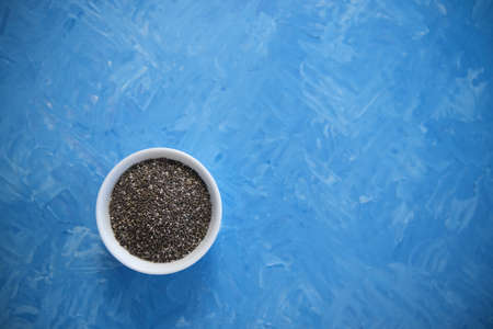 Chia seeds are organic food for a healthy diet. In a round bowl. The blue background is painted with oil paintsの写真素材