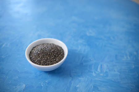 Chia seeds are organic food for a healthy diet. In a round bowl. The blue background is painted with oil paintsの写真素材