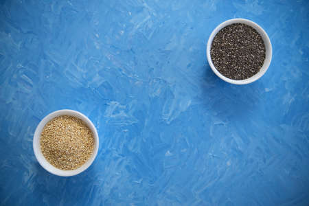 Quinoa and chia seeds are organic food for a healthy diet. In a round bowl. Two white cups. The blue texture is painted with blue oil paints.の写真素材