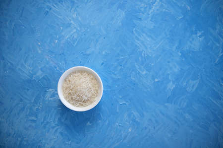 Rice is an organic food for a healthy diet. In a round bowl. The blue background is painted with oil paints.の写真素材