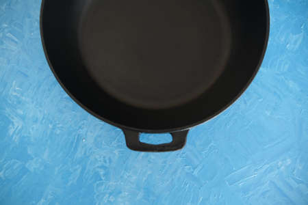 Empty cast-iron frying pan on a blue cooking background, top view. Oil painting.の写真素材