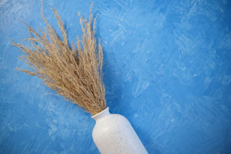 The composition consists of a white ceramic vase with a bouquet of dried spikelets, a golden photo...