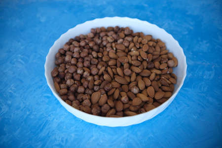 A wooden bowl with mixed nuts on top of a blue table. Healthy food and snacks. Nuts, pistachios, almonds, hazelnutsの写真素材