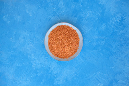 Red lentils close-up. Background with lots of lentils. Minimalism. Blue background. Top view. Soft...