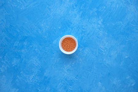 Red lentils close-up. Background with lots of lentils. Minimalism. Blue background. Top view. Soft...