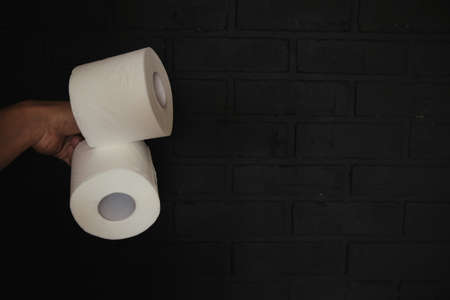 Toilet paper on a black brick background. The hand holds two rolls.の写真素材