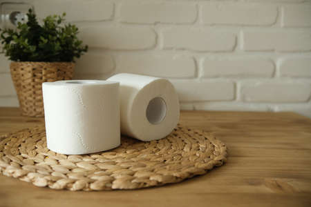 Toilet paper on a wooden table. Two white rolls. Brick background. A green flower. White and beige colors.の写真素材