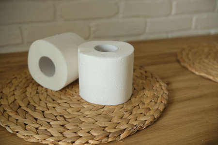 Toilet paper on a wooden table. Two white rolls. Round woven mat. Beige colors. White brick wall background.の写真素材