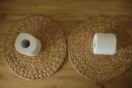 Toilet paper on a wooden table. Two white rolls. Round woven mat. White and beige colors. Top view.の写真素材