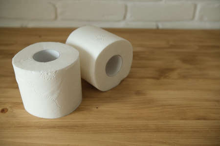 Toilet paper on a wooden table. Two white rolls. Beige colors. White brick wall in the background.の写真素材