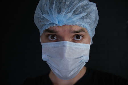 A doctor wearing a mask and  looks away. A surprised face. Close-up. Black backgroundの写真素材