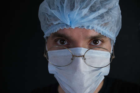 A doctor wearing a mask and glasses looks into the camera. Close-up. Black backgroundの写真素材