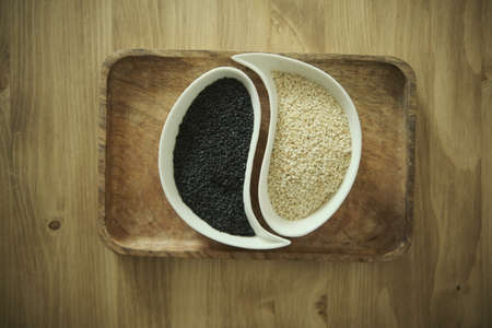 White sesame and black sesame seeds on a white plate. Wooden table. Soft selective blurred background.の写真素材